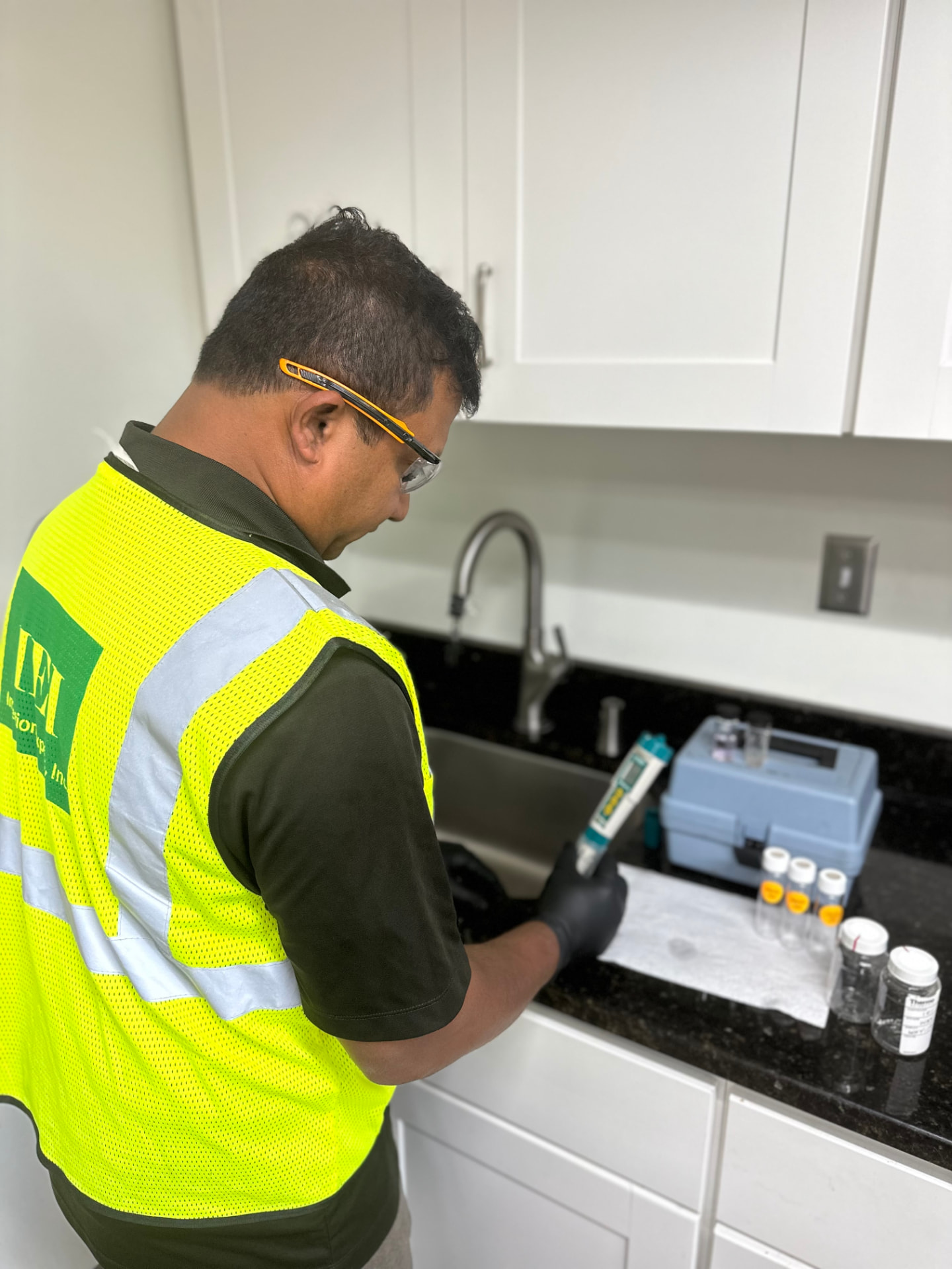 IEI technician in an IEI safety vest collecting a drinking water sample from a building sink
