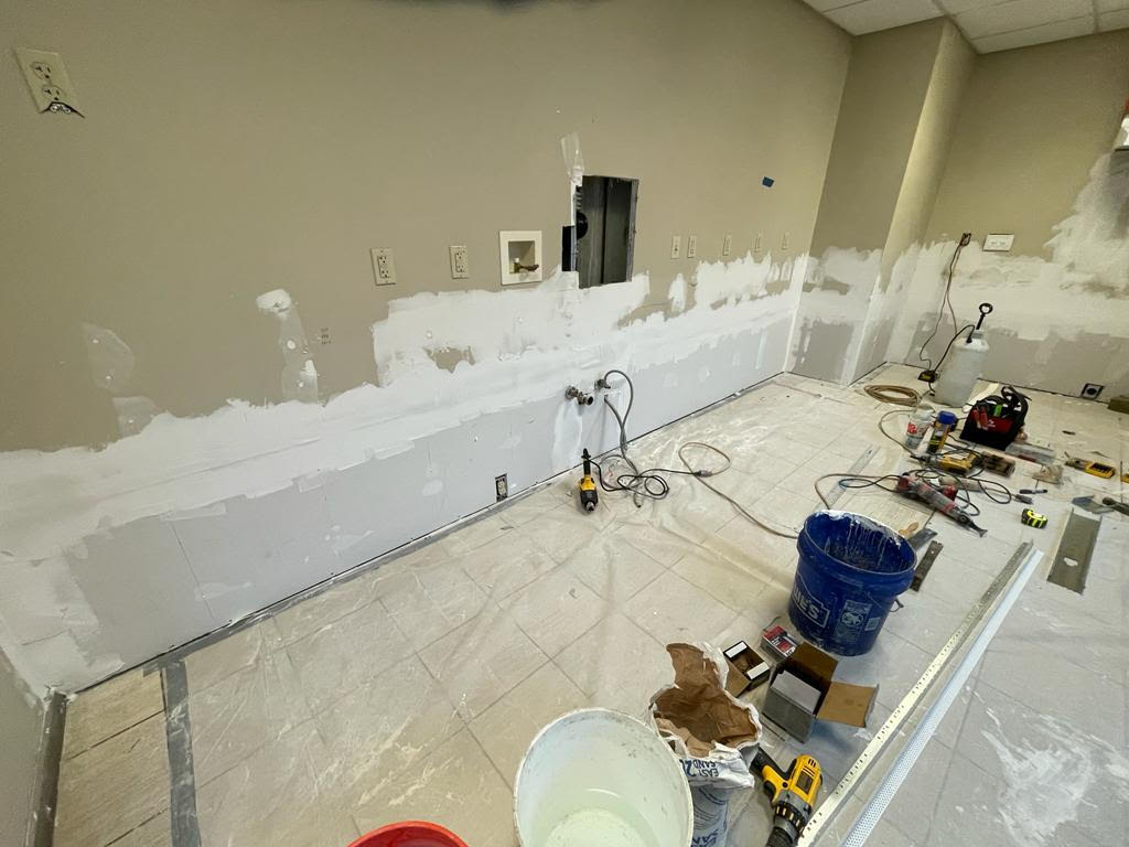 Interior room during renovation with wall repair, dust protection on the floor, and tools staged by IEI