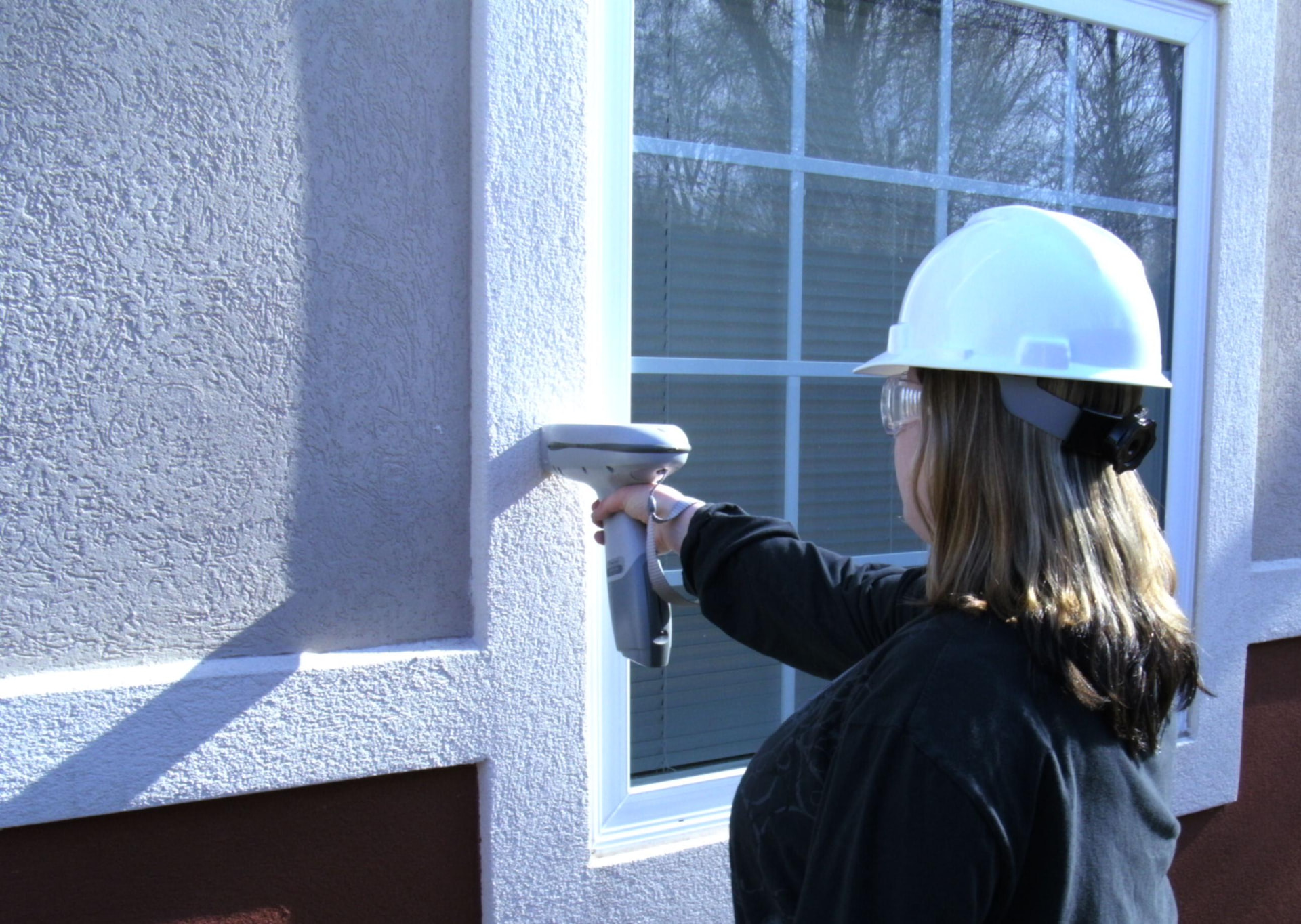 IEI inspector using a handheld XRF analyzer to screen a stucco wall near a window for lead-based paint