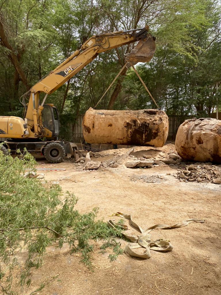 Excavator lifting a corroded underground storage tank out of an excavation during a tank removal