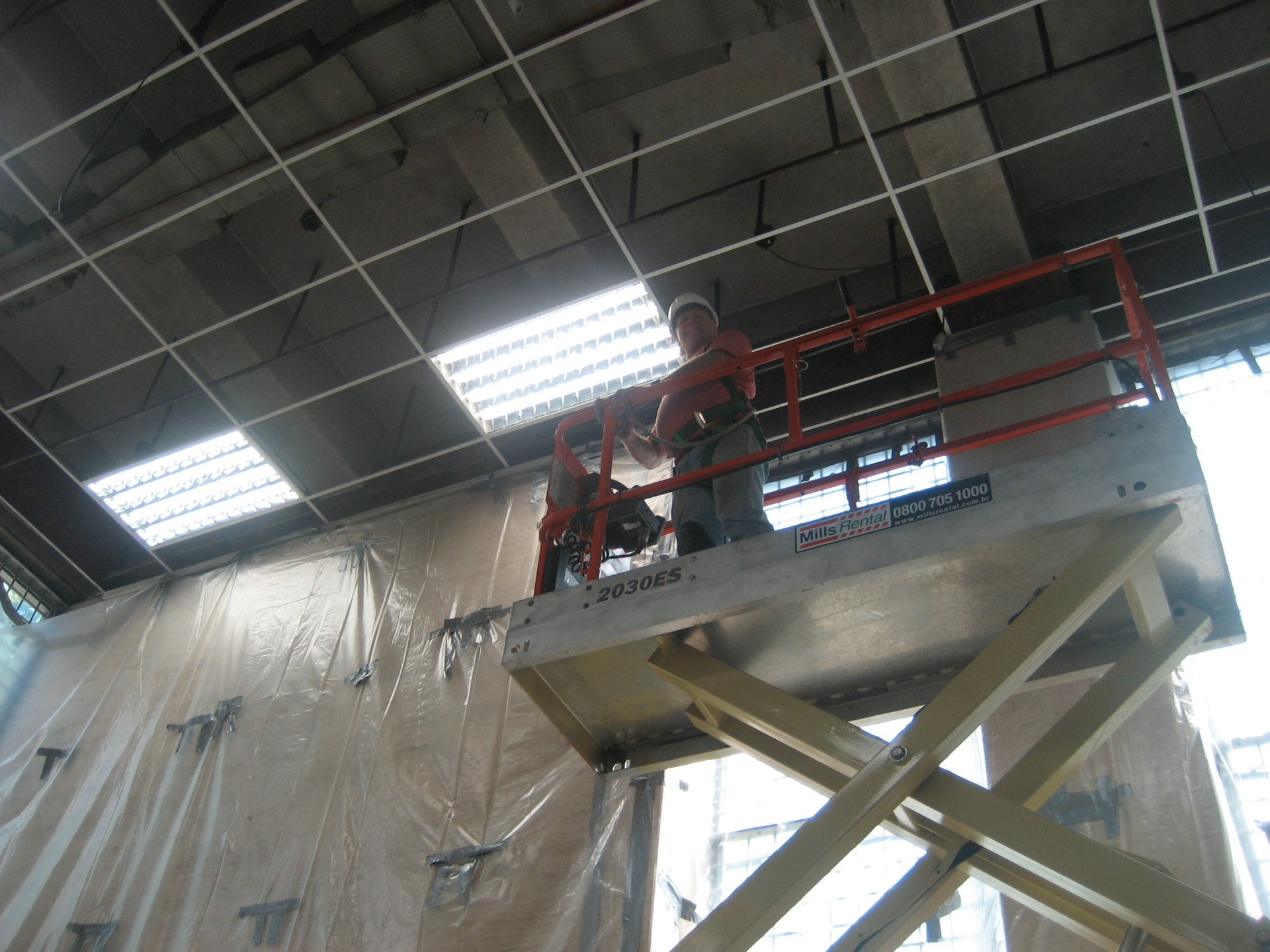 Worker on a scissor lift installing ceiling light fixtures beneath temporary dust protection