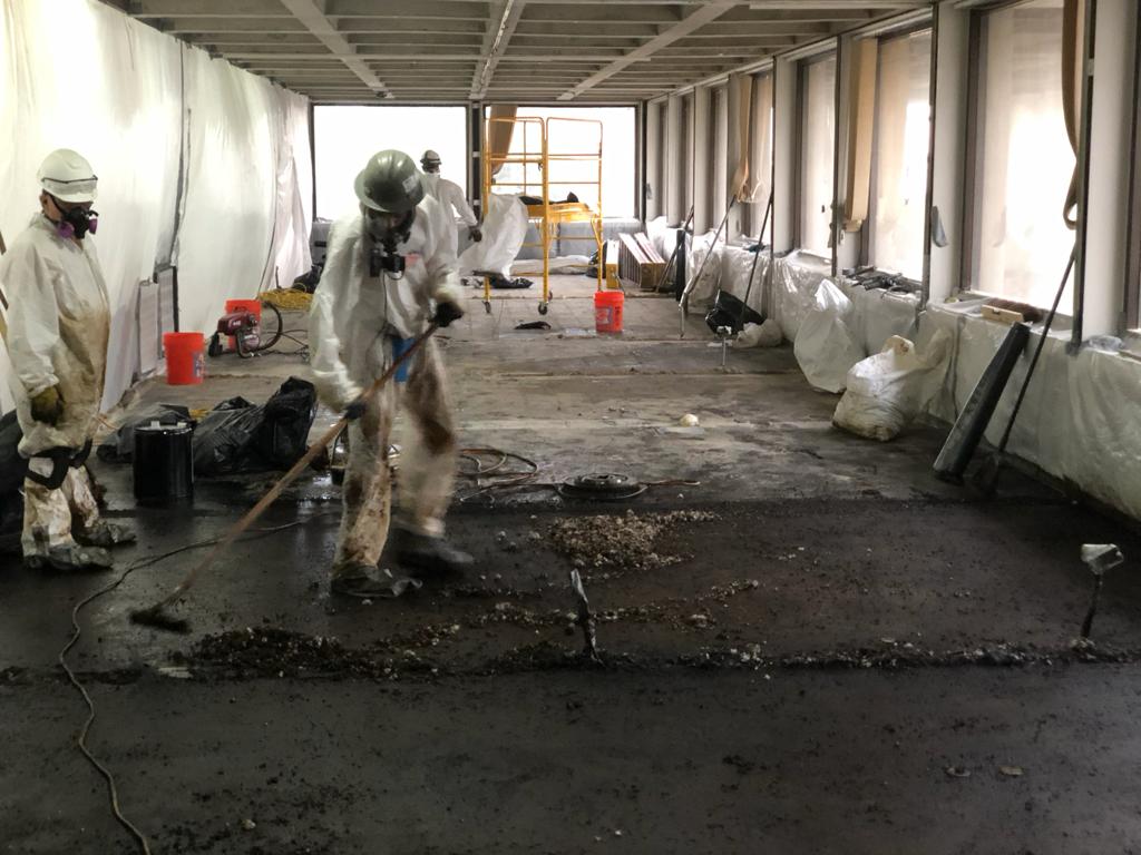 IEI crew in protective suits removing contaminated flooring inside a plastic-sheeted containment area